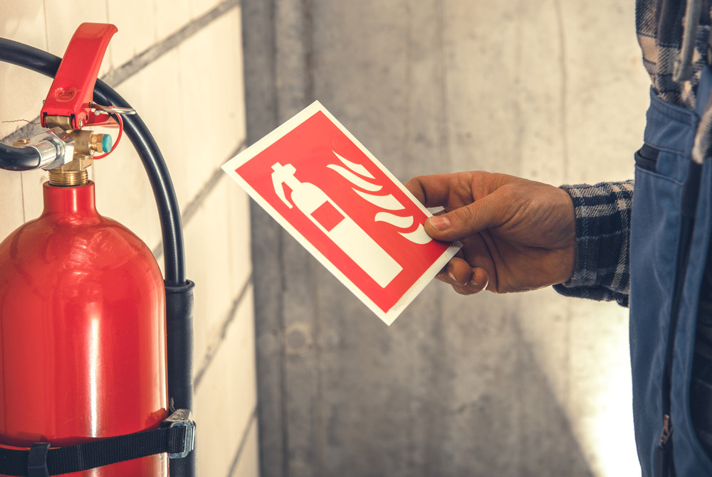 Fire Extinguisher and Required by Law Wall Sings Installation Inside Commercial Building by Caucasian Worker